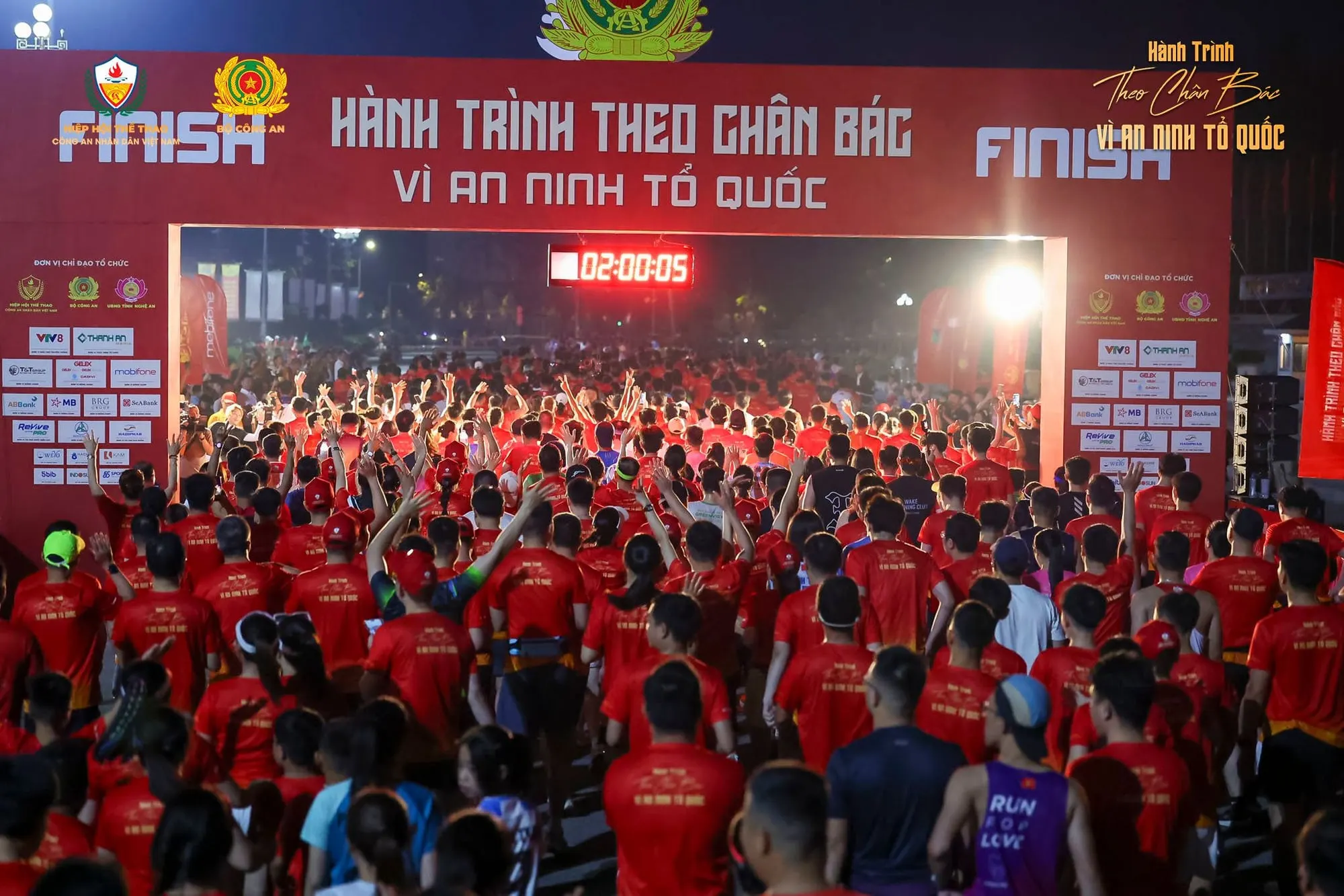 Hàng nghìn vận động viên áo đỏ dưới cổng xuất phát – về đích, đồng hồ 02:00:05