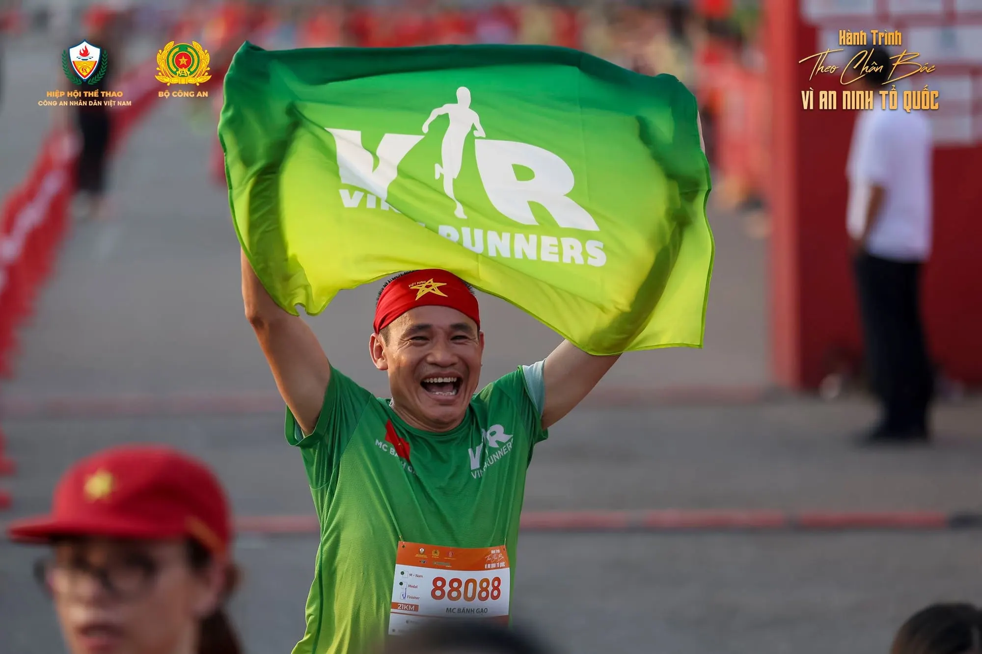 A runner holds a club flag high, laughing at the finish