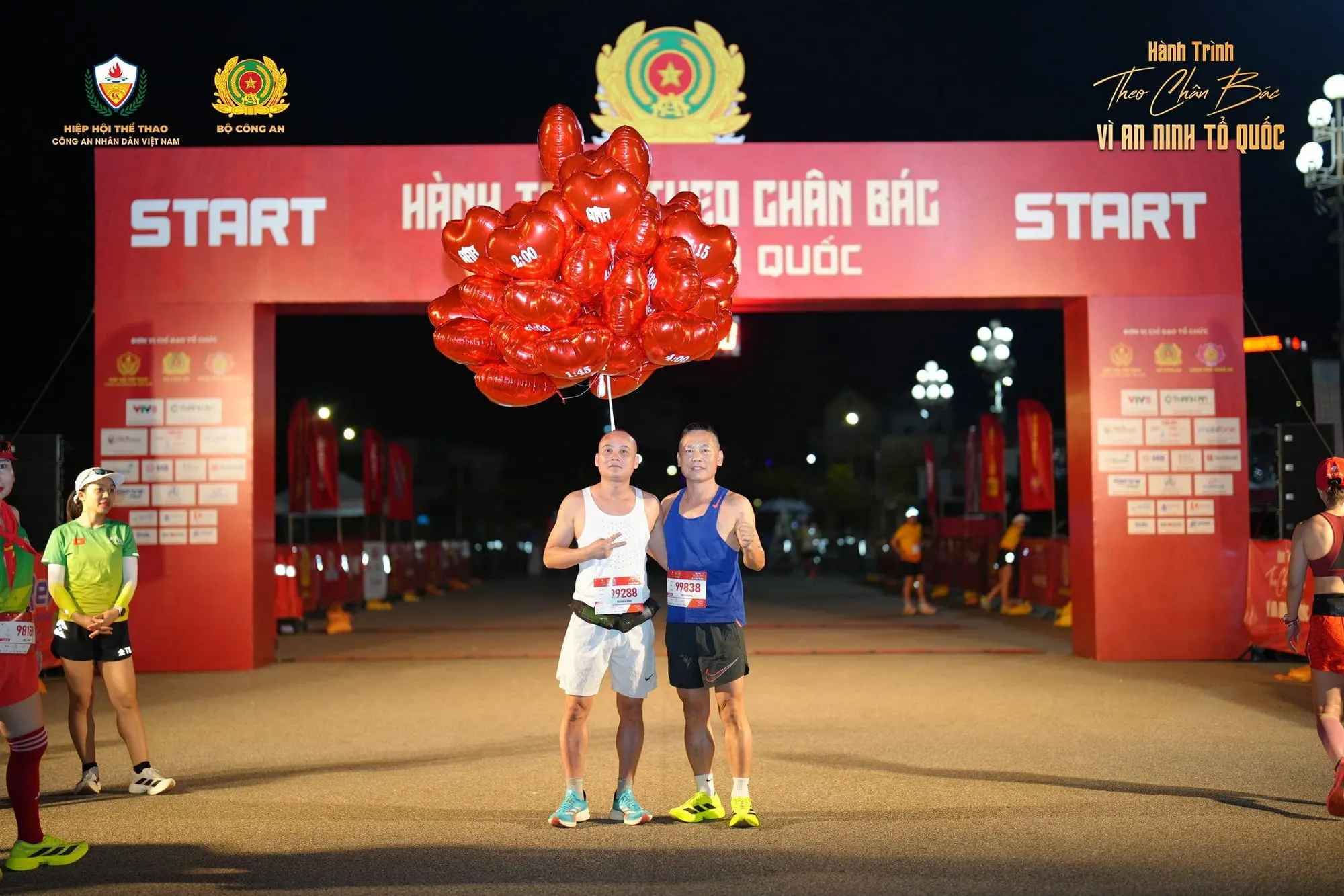 Two pacers holding red balloons under the START arch at night