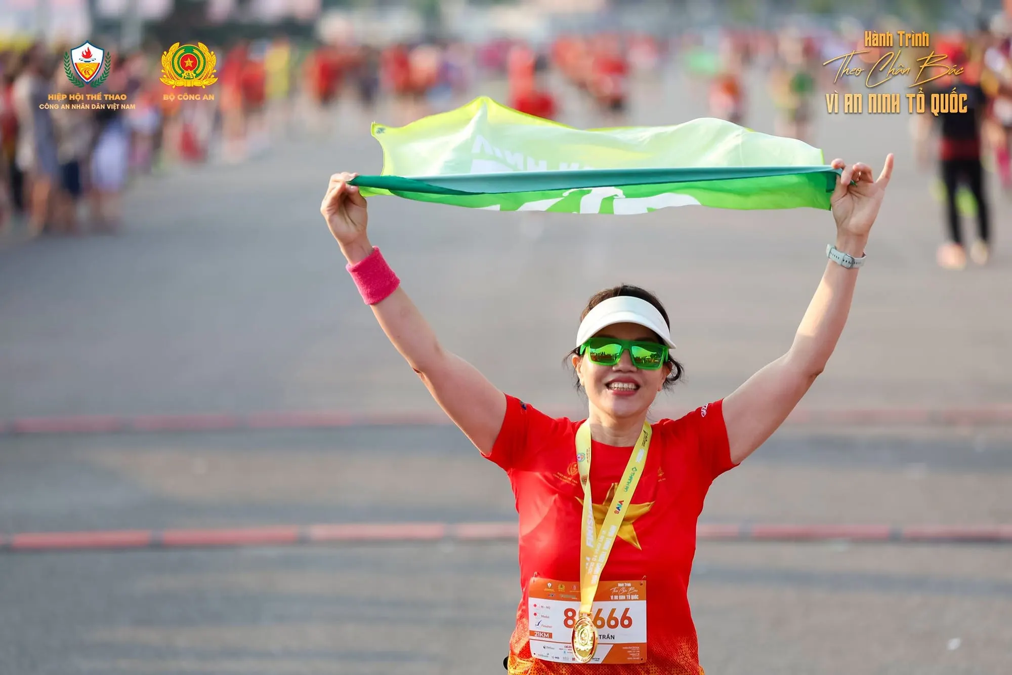A runner wearing her medal holds a scarf above her head
