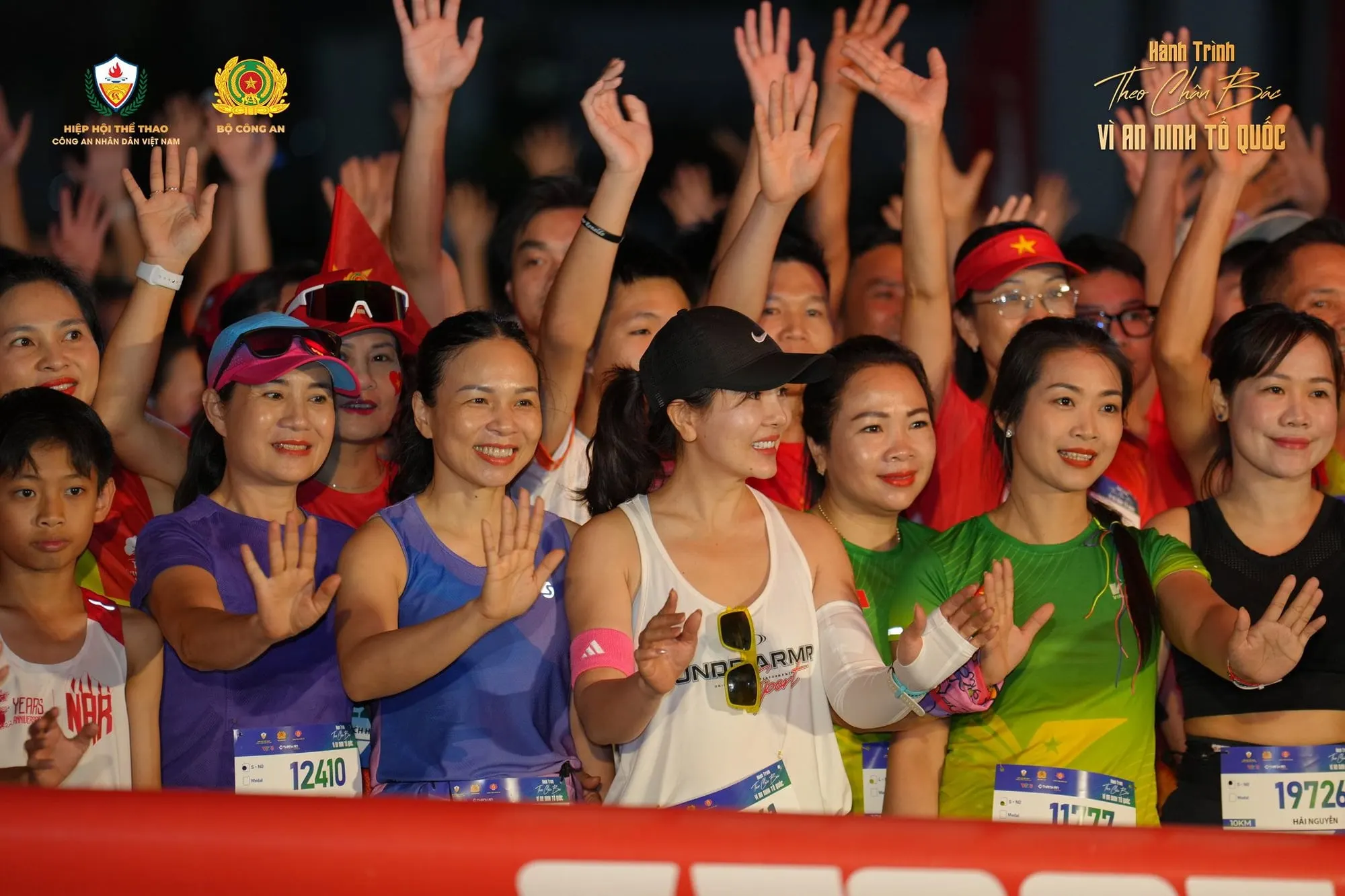 Front-row runners in bibs waving before the start at night