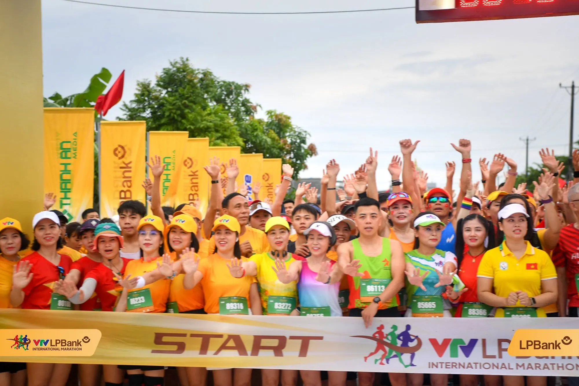 The front row in bibs raising their hands behind the START tape at daybreak