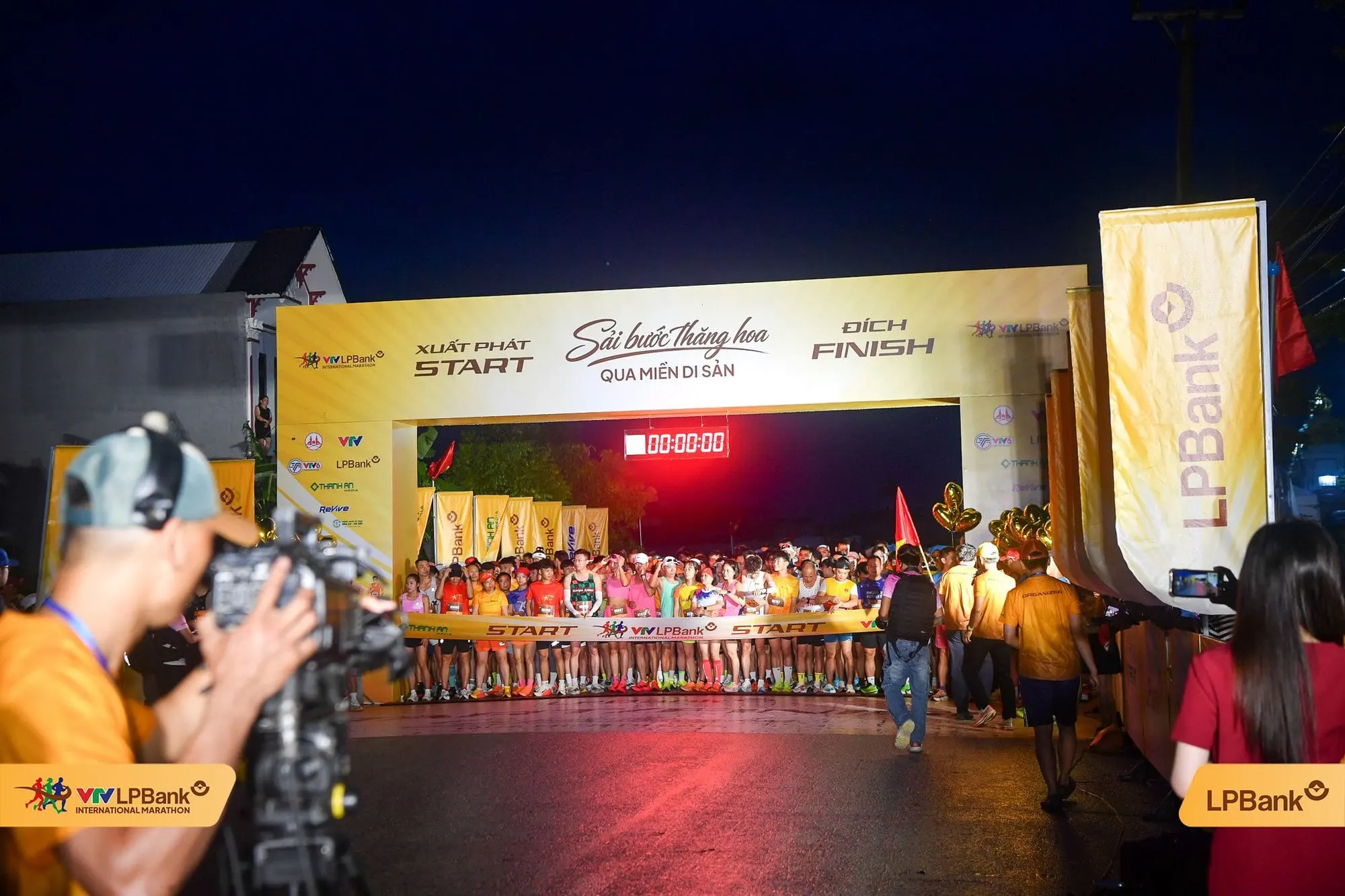 Photographers and camera crew at the lit start arch before dawn