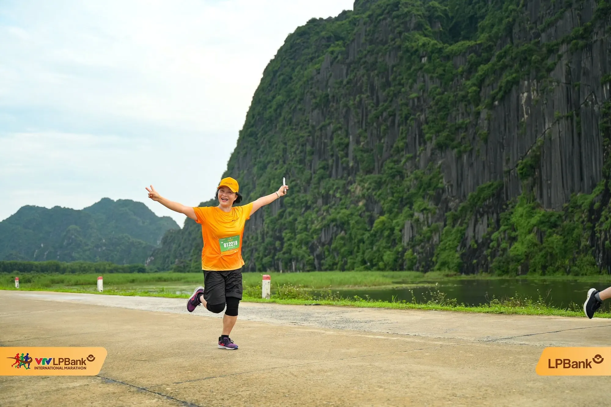 A runner with arms spread on a dyke road, limestone cliffs behind