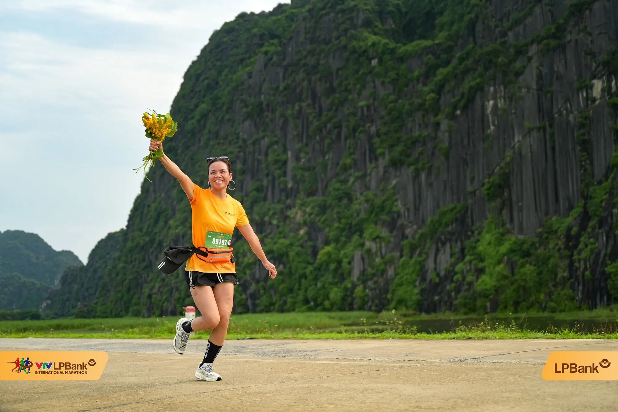 A runner holds up a bouquet, running below limestone cliffs