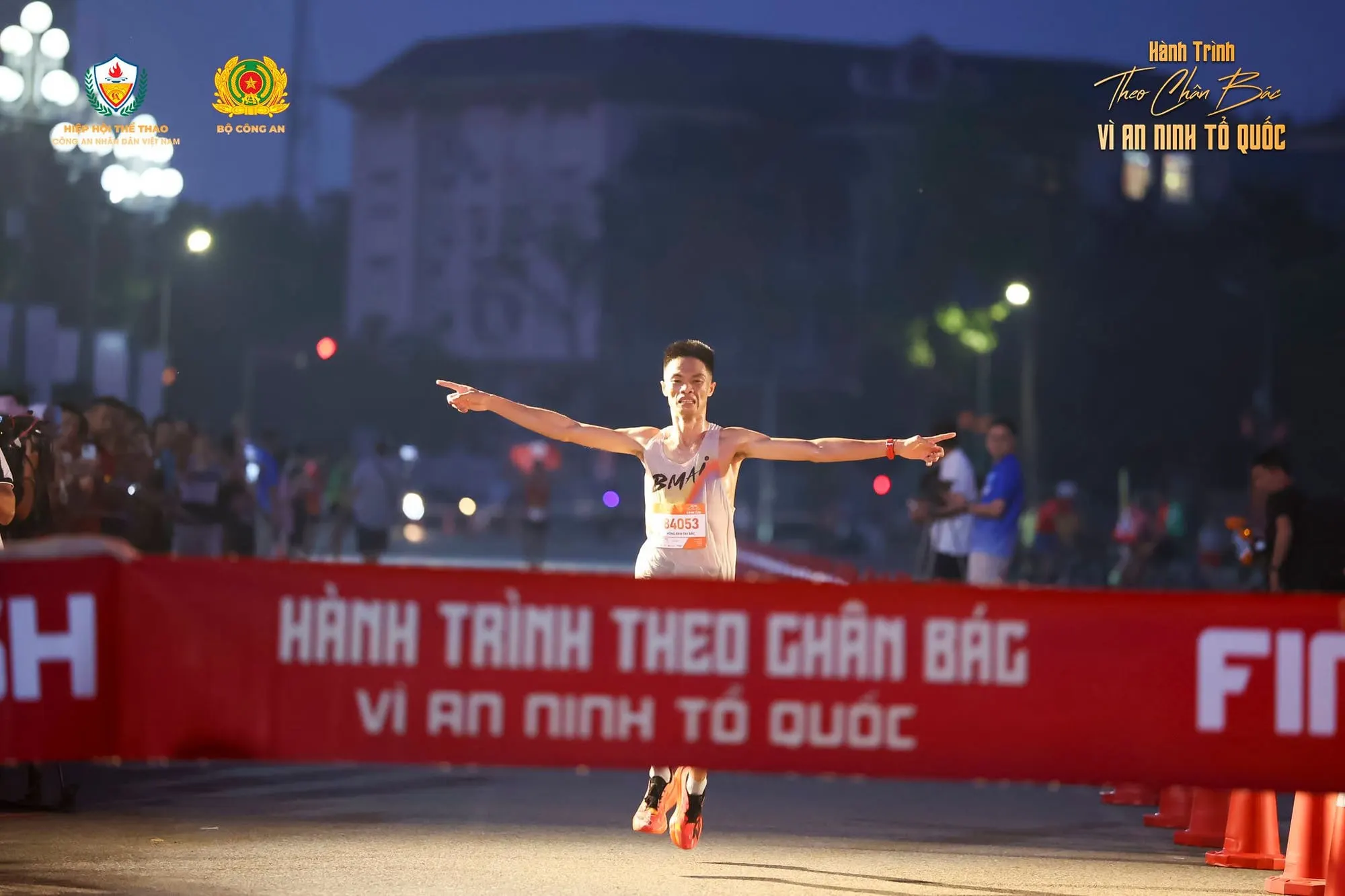 A runner spreads both arms as he breaks the finish tape at first light