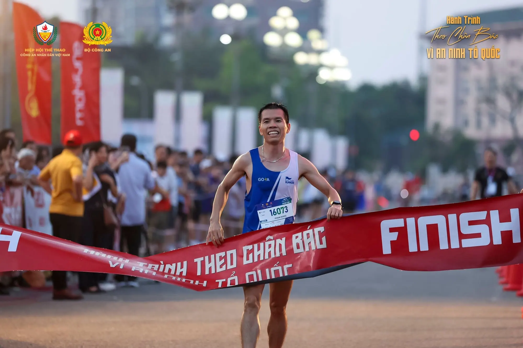 A runner in blue breaks the FINISH tape, spectators on both sides