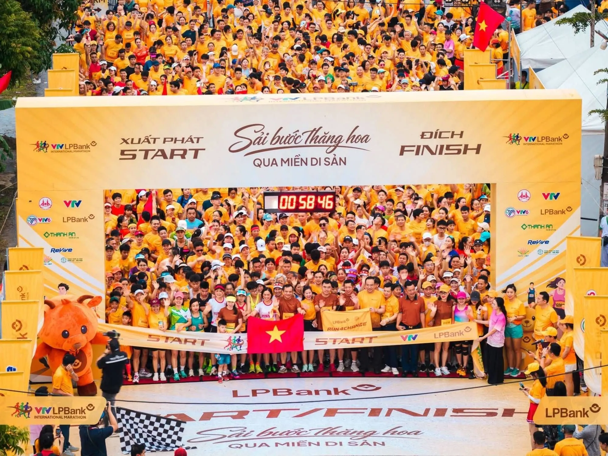 A sea of yellow shirts under the start arch, the front row holding red-star flags