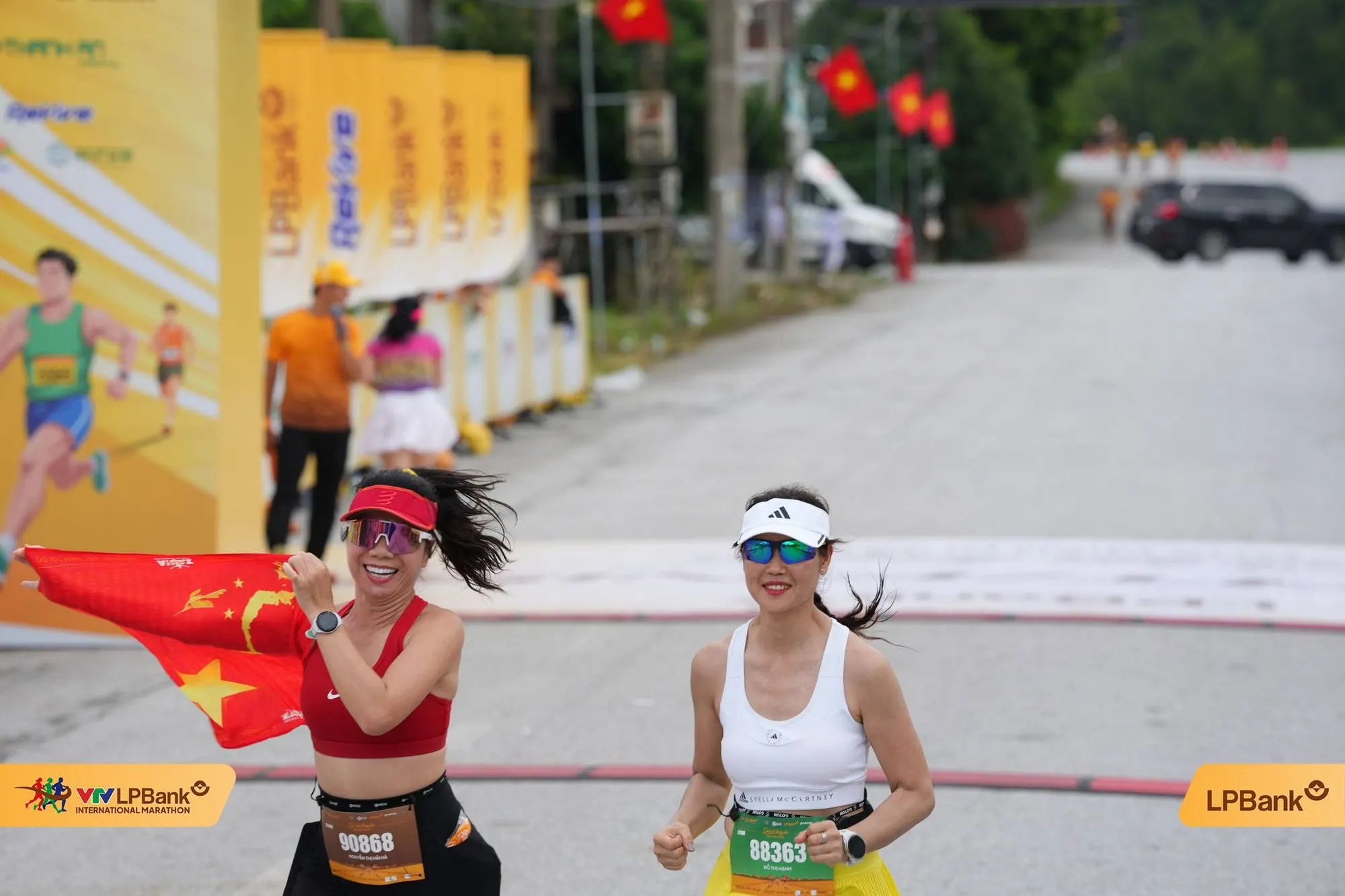 A runner carries a red-star flag to the finish alongside a friend