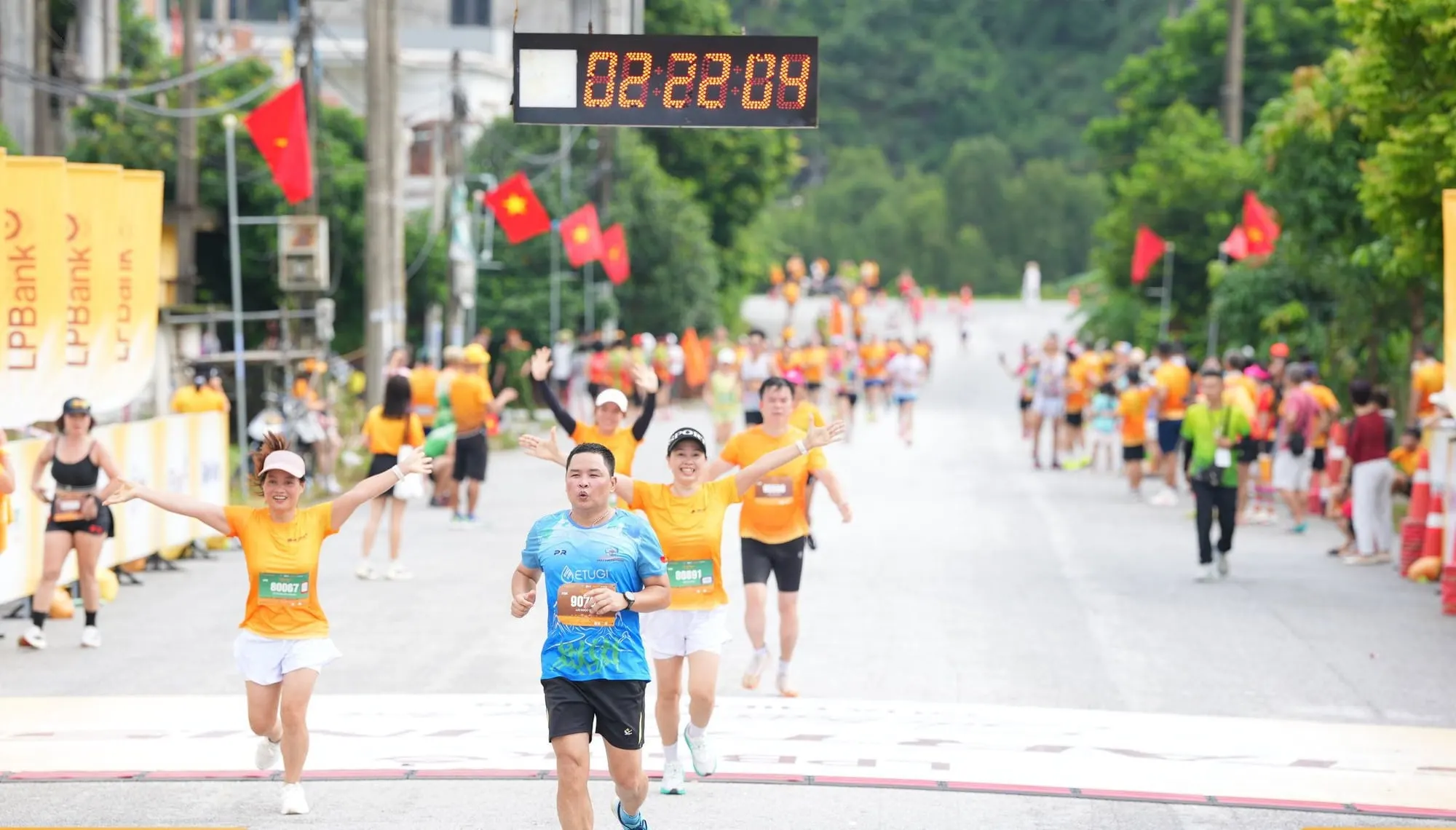 A runner crosses the finish with arms raised, clock at 02:22:04